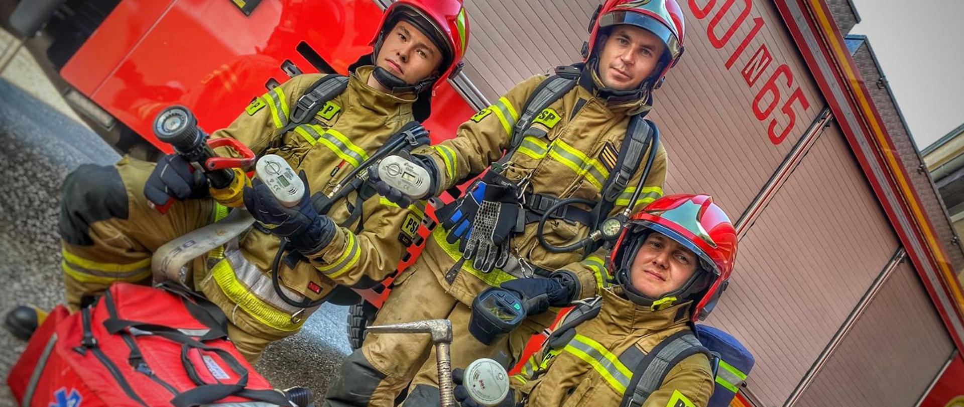 Zdjęcie ze strażakami, którzy trzymają czujki tlenku węgla i czujki dymu