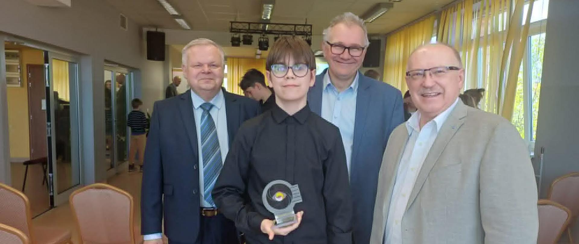 Uczeń w gronie Jury, trzyma nagrodę w postaci statuetki