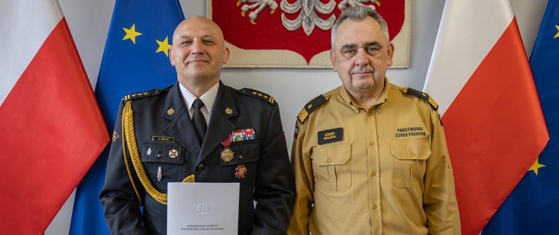Na zdjęciu komendnci stoją na tle godła i flag