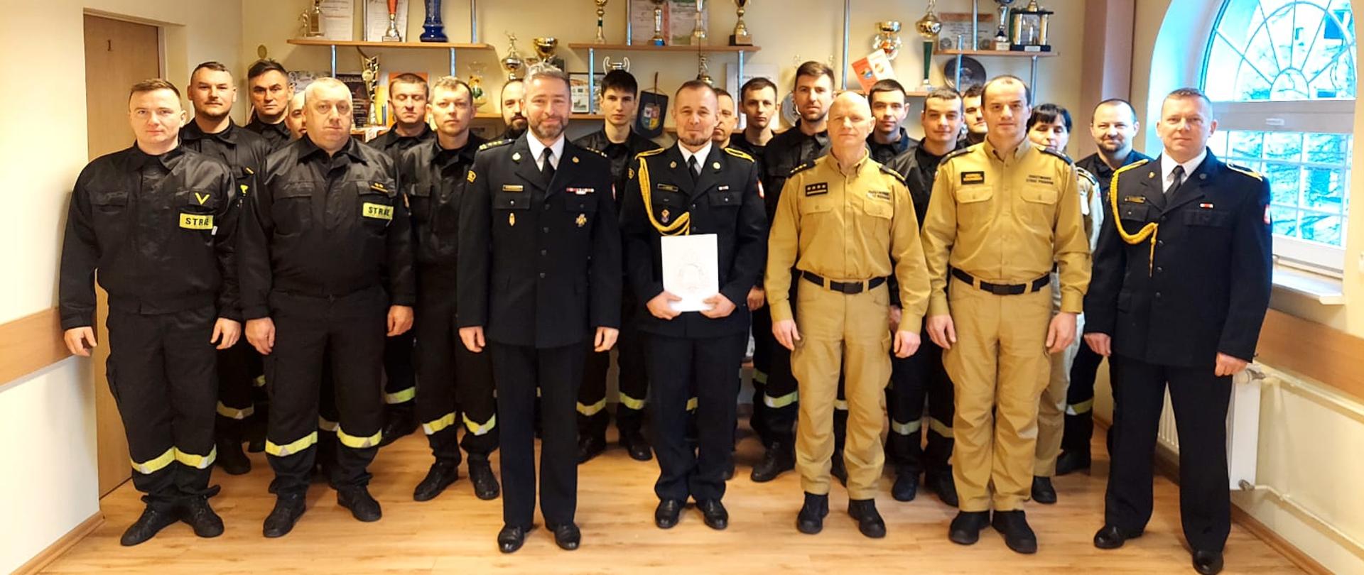 Na zdjęciu widoczne są wszystkie osoby biorące udział w apelu wraz ze strażakiem przechodzącym na zaopatrzenie emerytalne