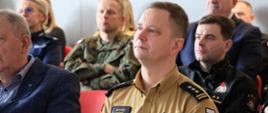 Narada roczna Komendy Miejskiej Państwowej Straży Pożarnej w Suwałkach - st. bryg. Marcin Wierel z zebranymi gośćmi słucha wystąpienia i prezentacji Komendanta Miejskiego w Suwałkach
