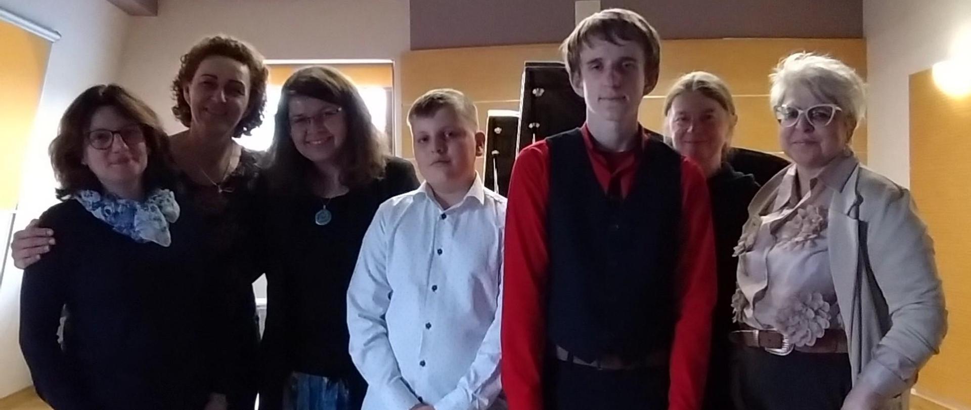 Zdjęcie z bliska na scenie sali kameralnej. Nauczycielki wraz z prowadzącą warsztaty oraz dwoma uczniami stoją w zwartym szyku