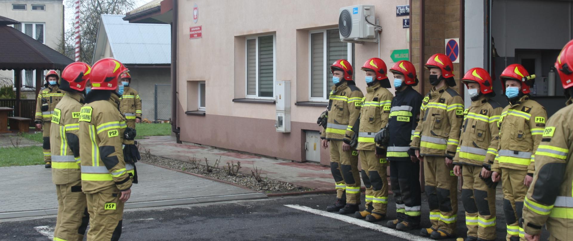 Zdjęcie przedstawia strażaków Jednostki Ratowniczo-Gaśniczej PSP w Lesku podczas uroczystej zbiórki z okazji Dnia Flagi Rzeczypospolitej Polskiej.