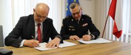 Kujawsko-pomorski komendant wojewódzki i Prezes WIOŚ podpisują dokumenty porozumienia. Rzecz dzieje się w gabinecie, przy stole, w tle flagi - narodowa i unijna.