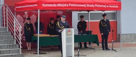 Zdjęcie przedstawia strażaków podczas obchodów dnia strażaka. Komendant przemawia przy mównicy. 