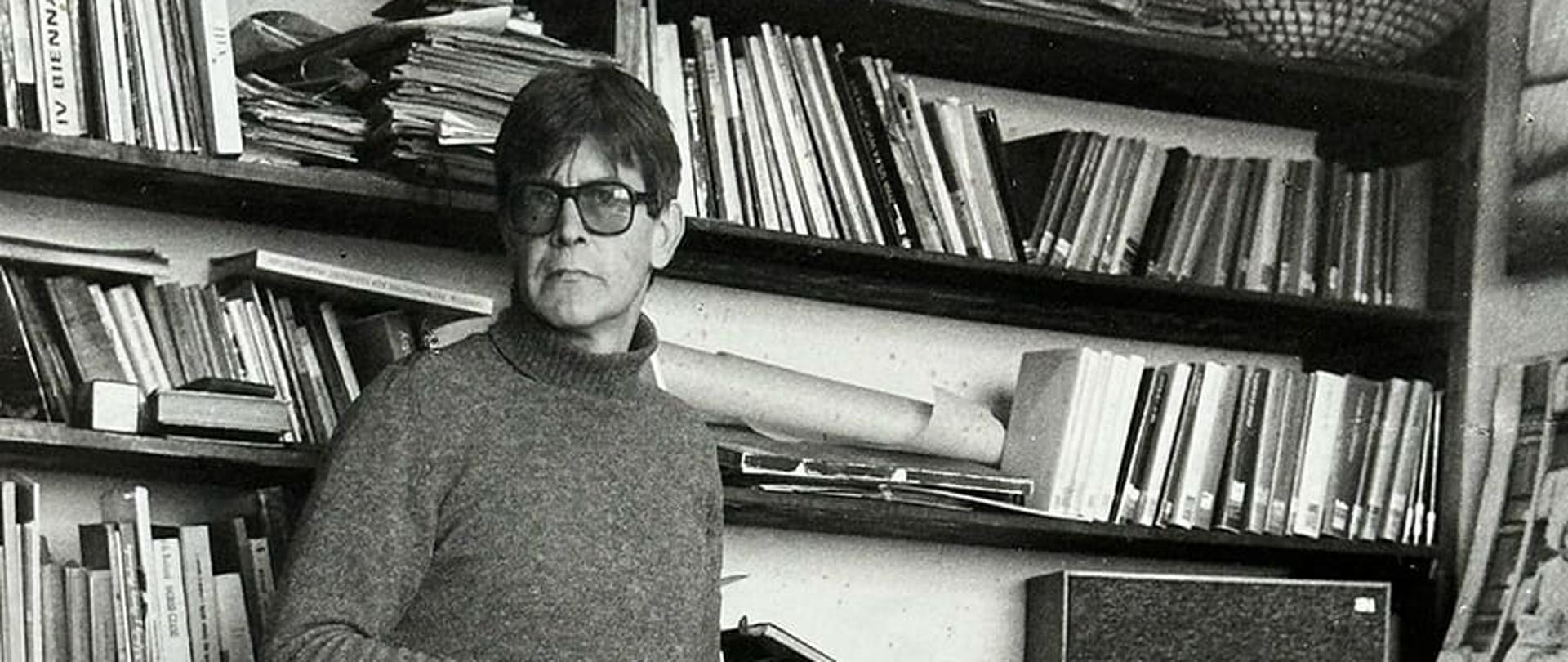 Profesor Stanisław Kluska - zdjęcie historyczne. Profesor na tle pracowni - półki z książkami w tle.