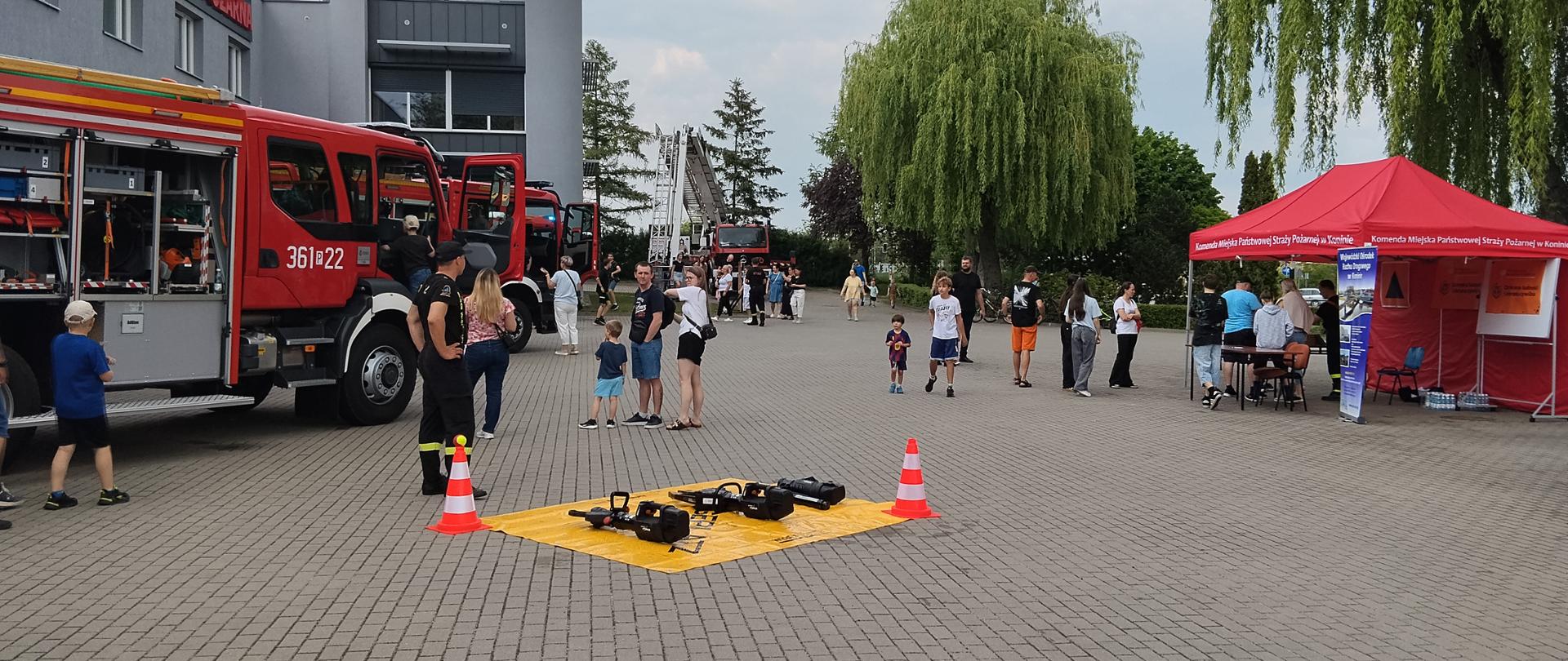Piknik bezpieczeństwa u konińskich strażaków. Samochody strażackie stoją przed budynkiem. Strażacy prezentują sprzęt ratowniczo-gaśniczy