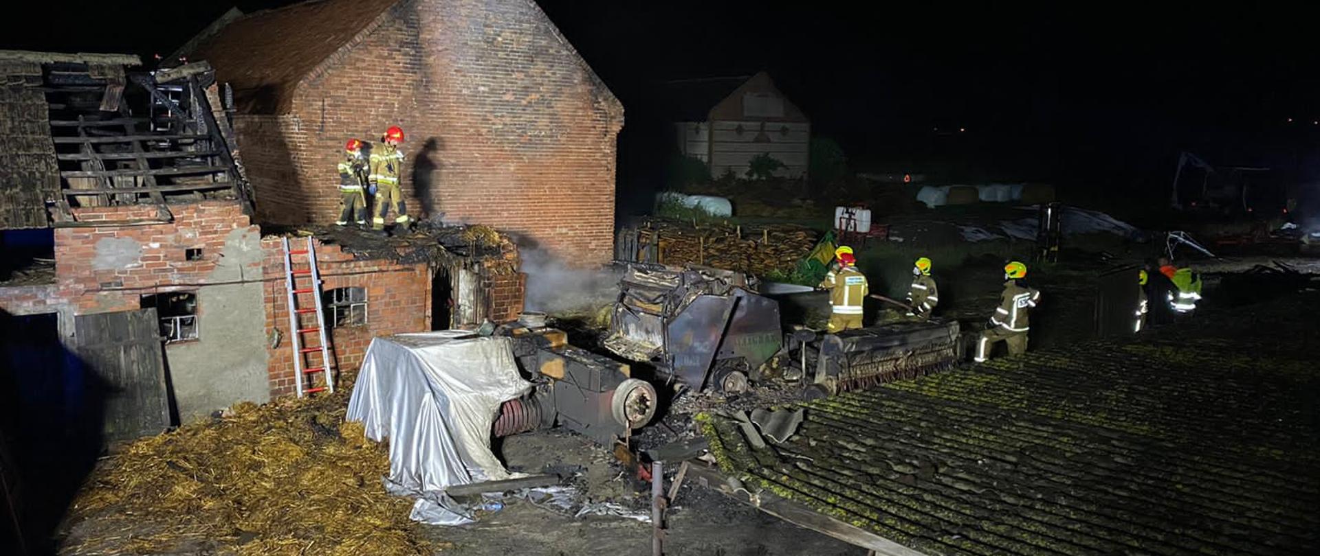 Zdjęcie przedstawia strażaków prowadzących prace rozbiórkowe na budynku inwentarskim, który uległ spaleniu. 