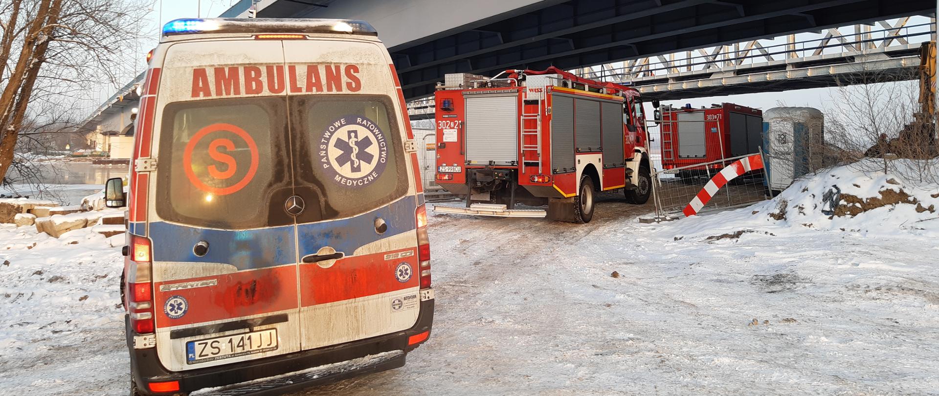 Karetka oraz pojazdy Państwowej Straży Pożarnej stojące przy nabrzeżu nieopodal miejsca zdarzenia