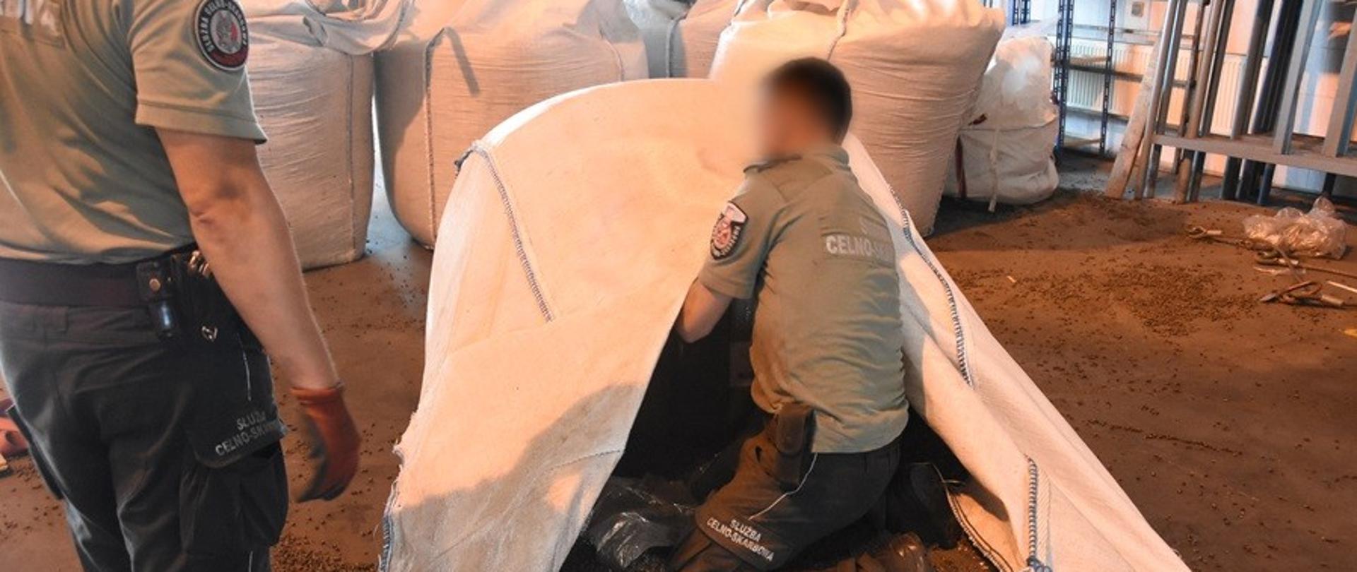 Dwóch funkcjonariuszy sprawdza zawartość dużego białego worka; wokół stoją kolejne worki.