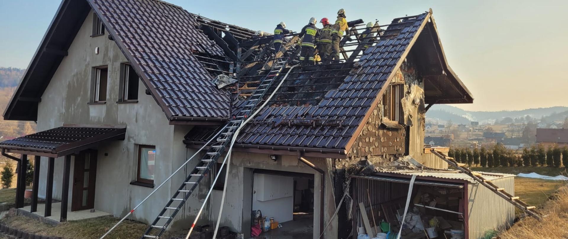 Zdjęcie przedstawia strażaków pracujących na dachu budynku mieszkalnego. 