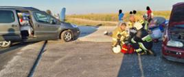 Na zdjęciu znajdują się samochody osobowe po uprzednim zderzeniu. Między samochodami znajdują się strażacy podczas akcji ratunkowej.