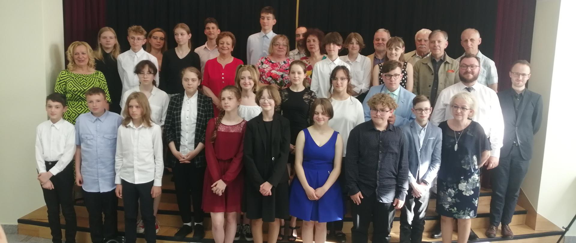 Zakończenie roku szkolnego absolwentów PSM I st. - w rzędach ustawieni nauczyciele i uczniowie