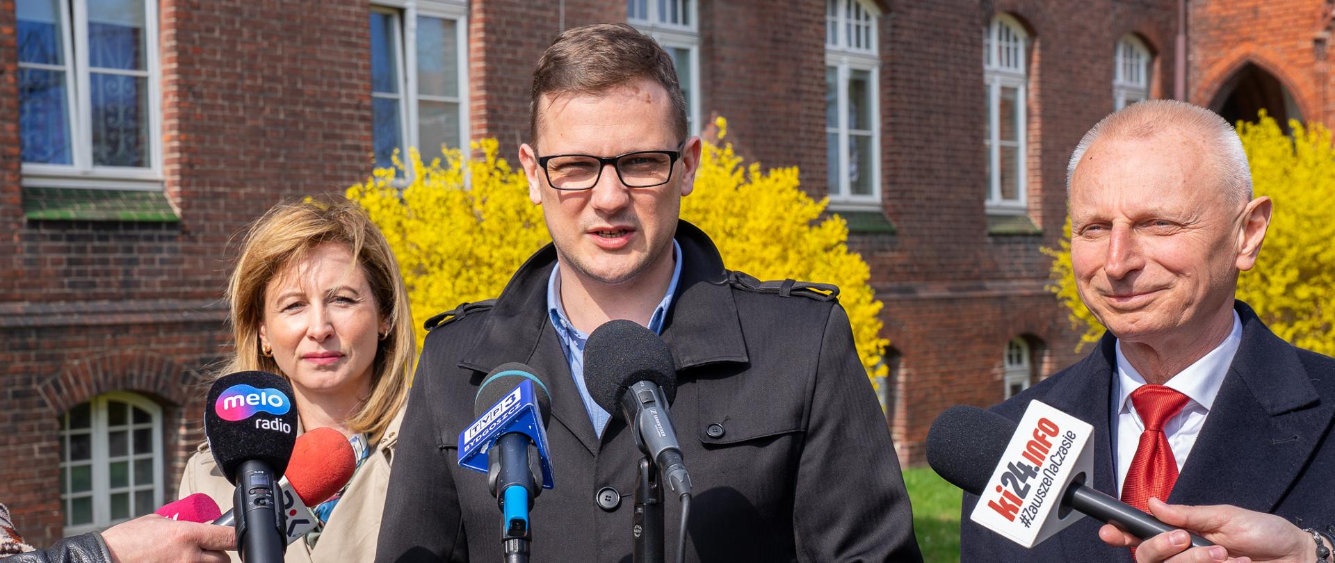 Wojewoda Kujawsko-Pomorski Michał Sztybel wypowiada się podczas konferencji dotyczącej wznowienie działalności inowrocławskiego punktu paszportowego. Obok niego stoi Senator Ryszard Brejza oraz Posłanka Magdalena Łośko.
