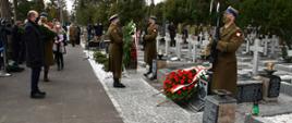 Zdjęcie przedstawia moment składania biało-czerwonych wieńców przed pomnikiem upamiętniającym żołnierzy Zgrupowania AK "Gurt". Tuż przy nim wartę pełnią żołnierze Wojska Polskiego, a tuż przed pomnikiem lezą biało-czerwone wieńce.