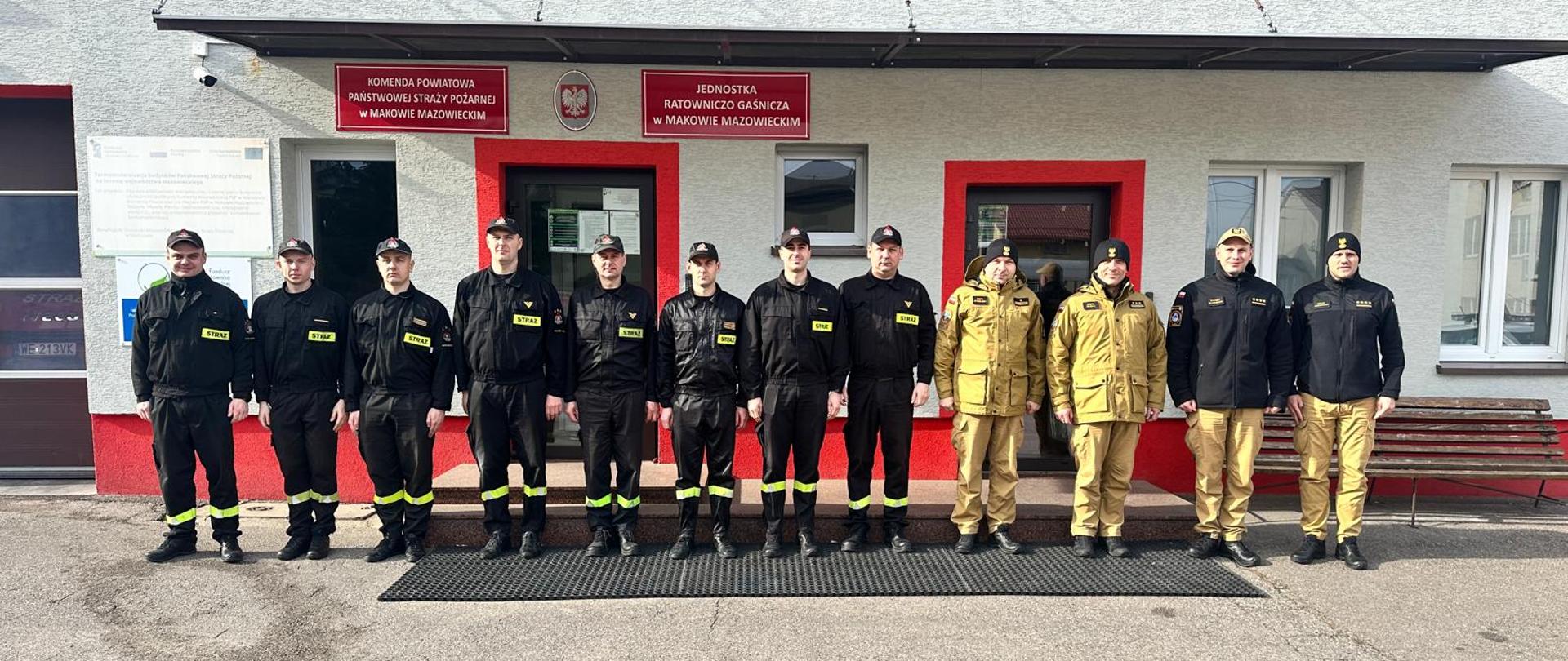 Dwunastu strażaków ustawionych w szeregu przed budyniem komendy powiatowej Państwowej Straży Pożarnej