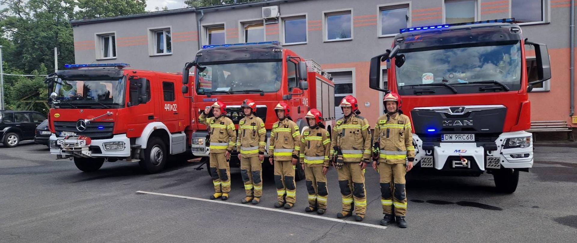 Obraz przedstawia strażaków Jednostki Ratowniczo-Gaśniczej w Jaworze podczas upamiętnienia 78. rocznicy wybuchu Powstania Warszawskiego. W tel samochody pożarnicze i budynek komendy.