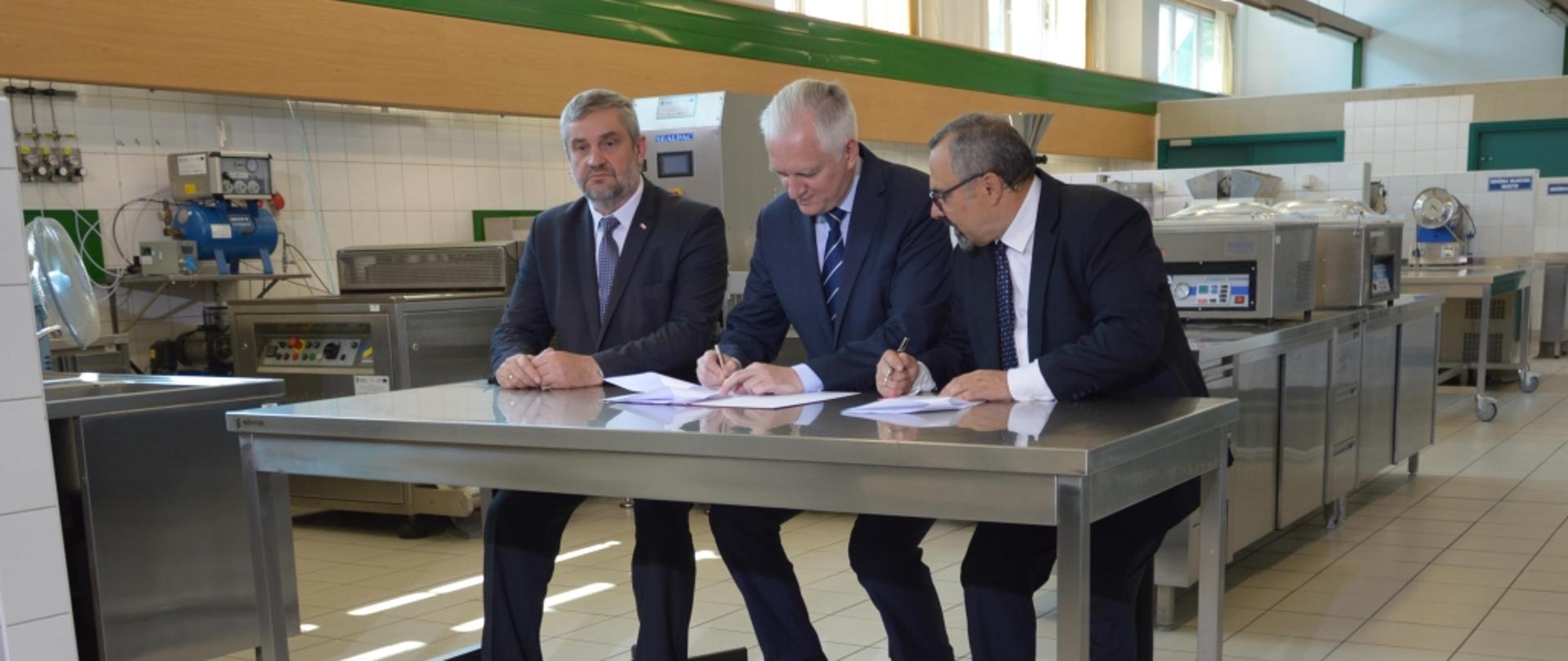 Ministrowie nauki i rolnictwa, oraz rektor SGGQW siedzą za stołem. Minister Gowin podpisuje umowę.