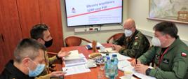 Przy stole podczas rozmów o współpracy siedzą dwaj funkcjonariusze PSP (po lewej) i dwaj przedstawiciele Sił Zbrojnych RP (po prawej) , na wprost na ścianie wisi ekran z napisem Obszary współpracy SZRP oraz PSP