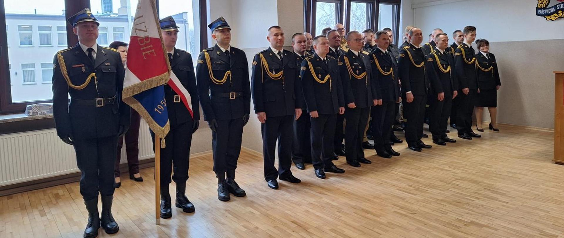 Poczet sztandarowy i strażacy w umundurowaniu galowym stojący w szeregu