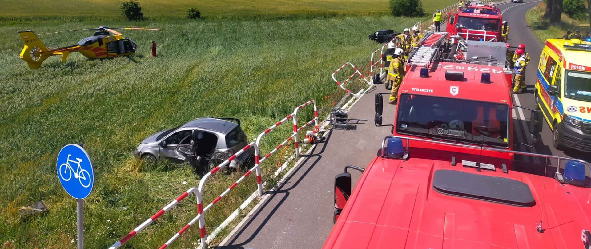 Zdjęcie zrobione z dachu samochodu pożarniczego. Na zdjęciu widać cały teren akcji – samochody pożarnicze, karetkę, śmigłowiec LPR, strażaków oraz pojazdy biorące udział w zdarzeniu.