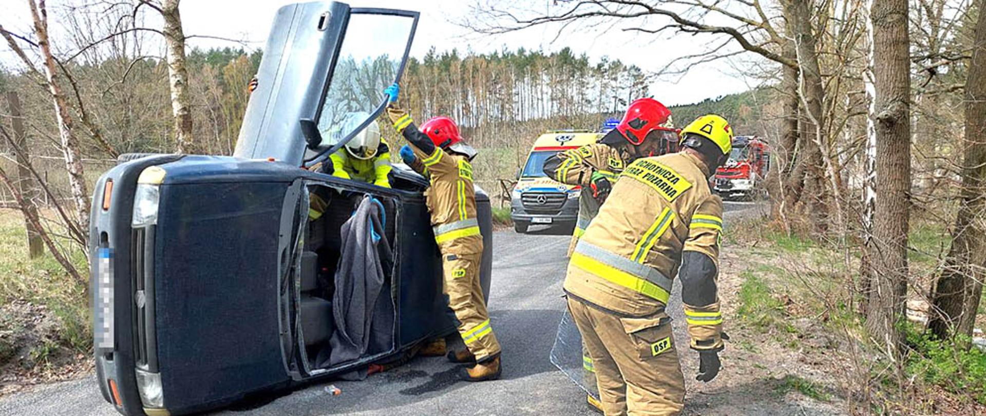 Pojazd leżący na boku oraz strażacy podczas działań ratowniczych.
