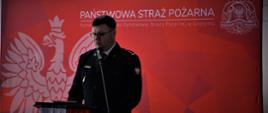 Zdjęcie przedstawia Zastępcę Wielkopolskiego Komendanta Wojewódzkiego PSP w Poznaniu przemawiającego do zaproszonych gości. Stoi on przy mównicy, słowa przekazuje przez mikrofon.