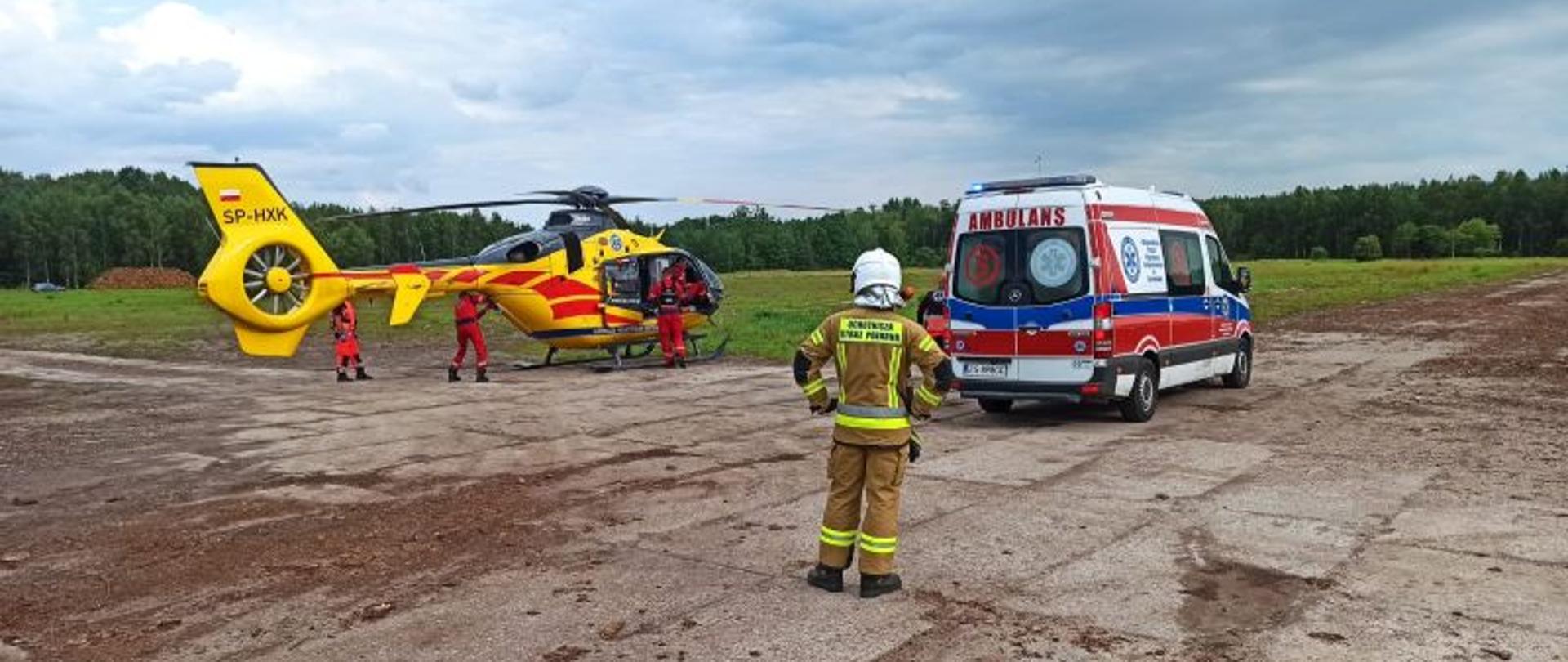 Zdjęcie przedstawia helikopter LPR, pogotowie oraz strażaków. Jest to miejsce lądowania maszyny.