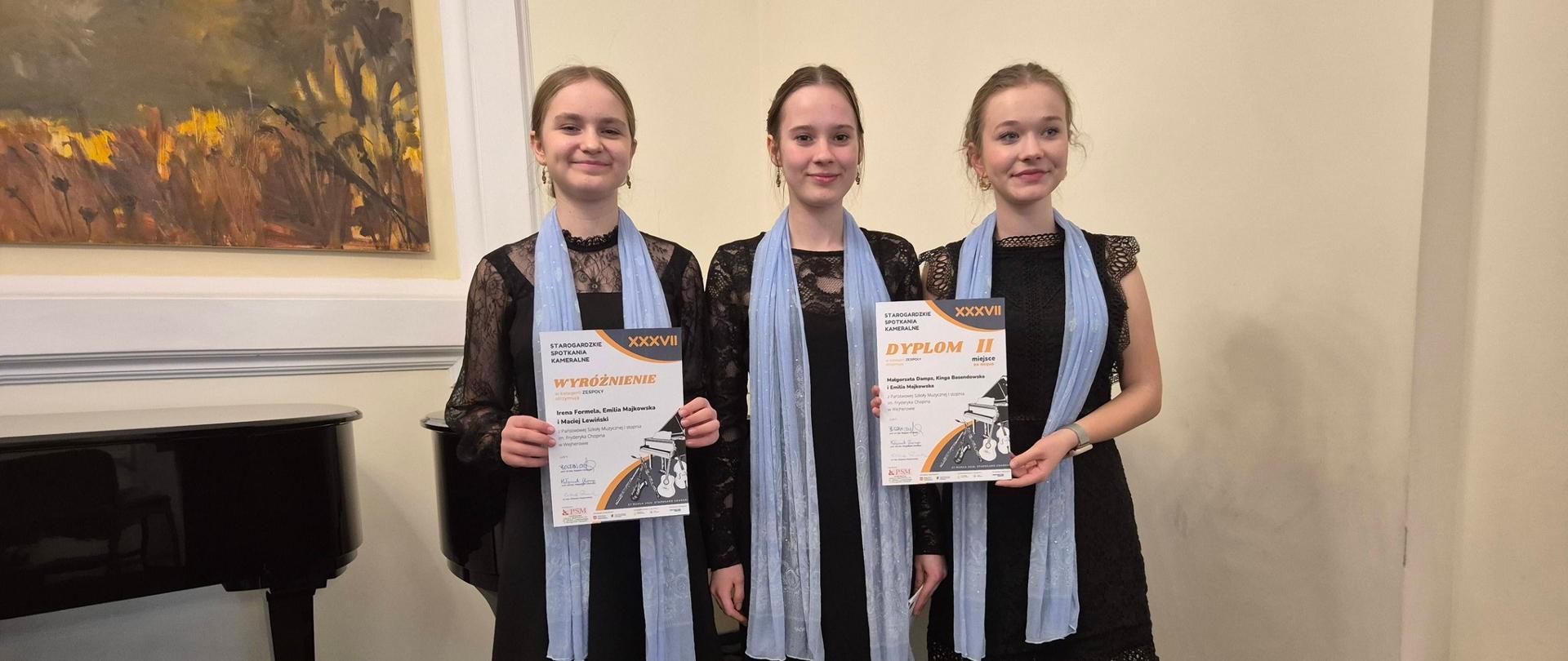 Uczennice trio klarnetowego pozują stojąc wraz z otrzymanymi dyplomami laureata