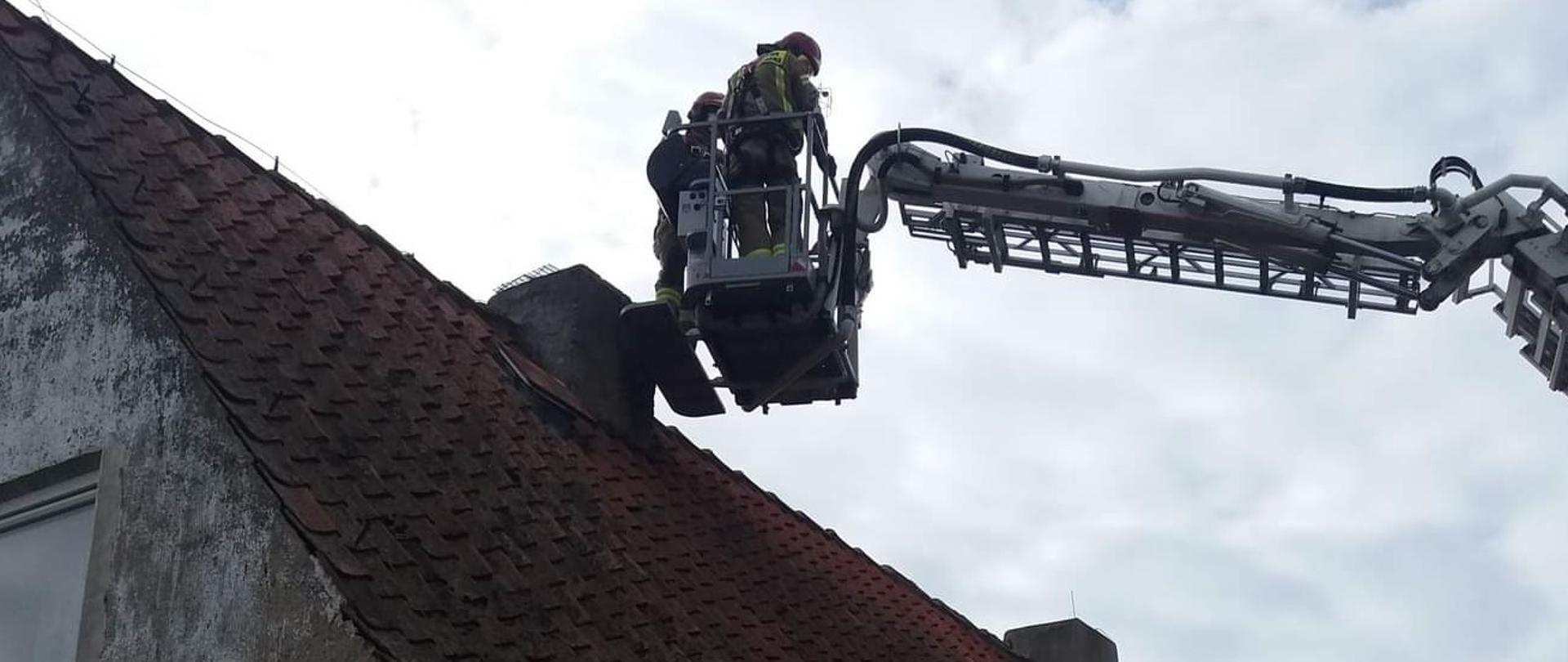 Strażacy w koszu podnośnika nad kominem 