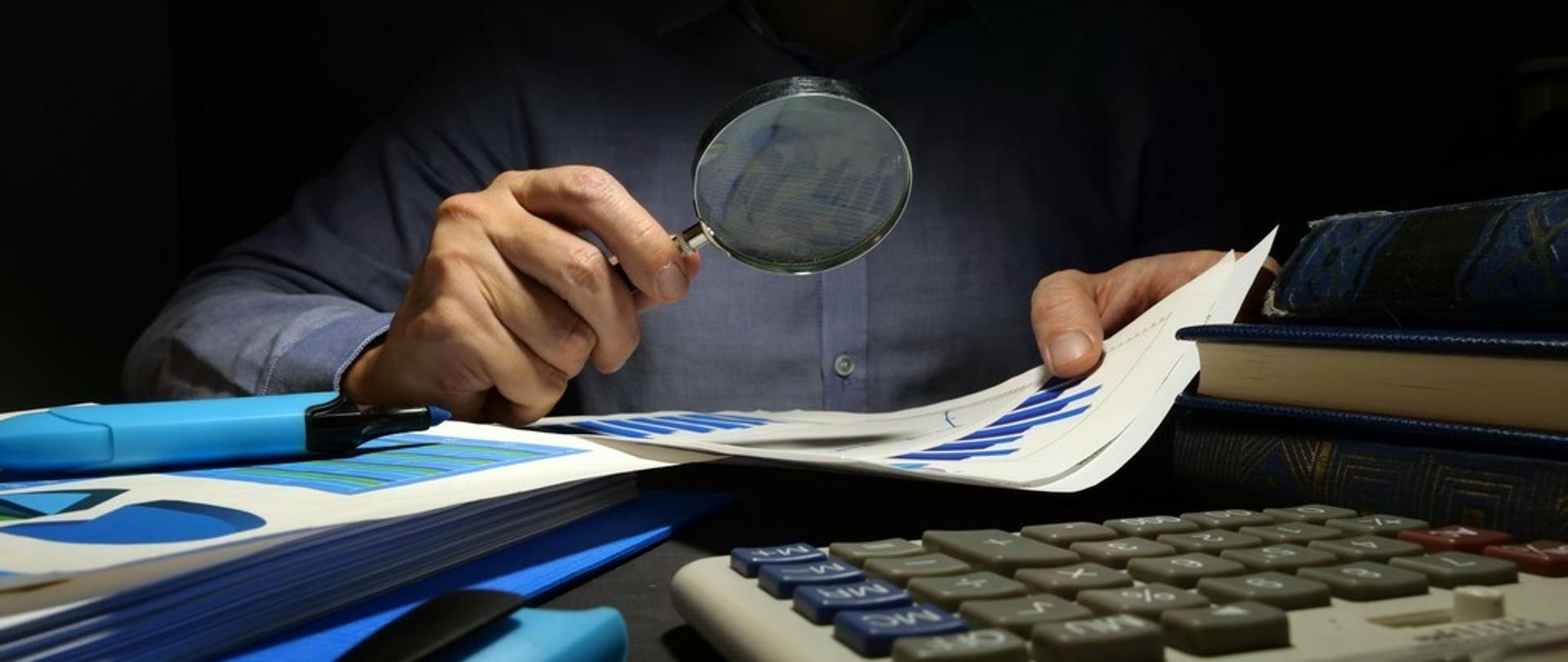 Kontroler analizuje dokumenty z wykresami przez szkło powiększające