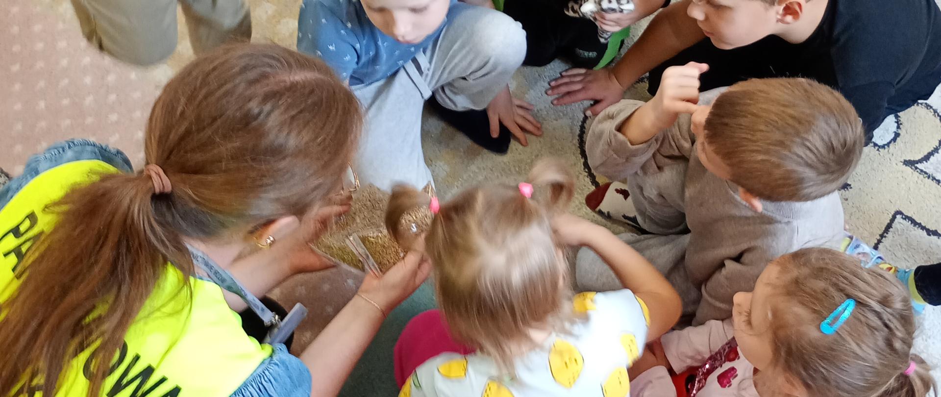 Inspektor trzymający woreczek z nasionami oraz uczestnicy spotkania na sali przedszkolnej. 