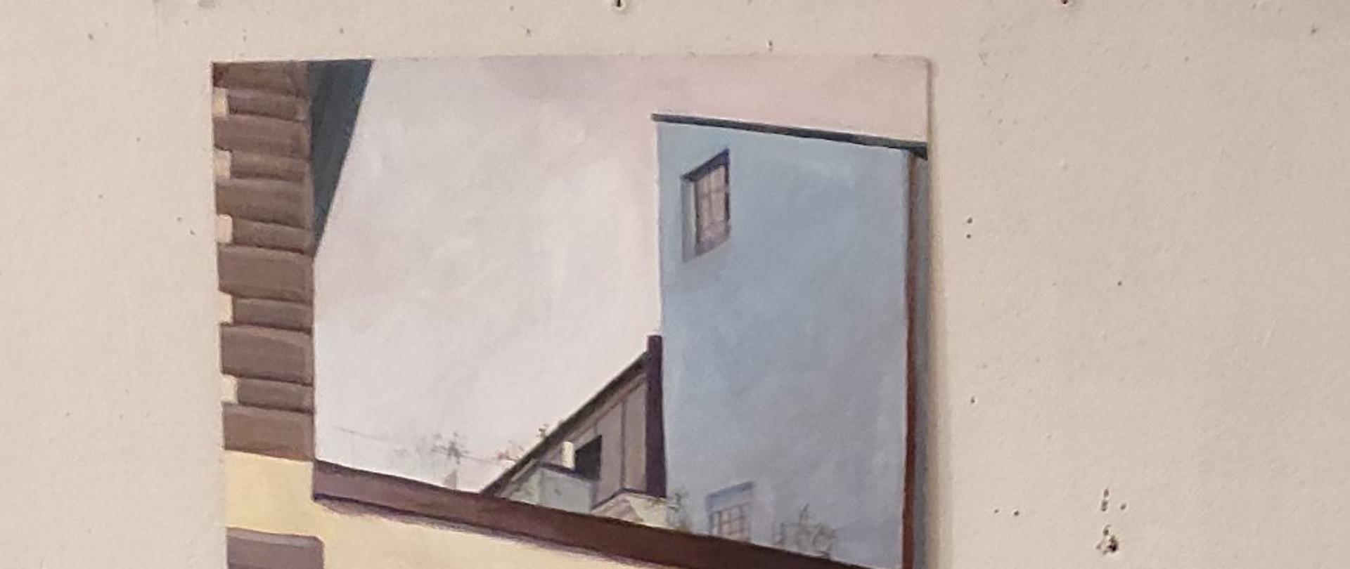 Aleksandra Suwaj na tle swojej pracy malarskiej. Praca przedstawia miejska zabudowę.