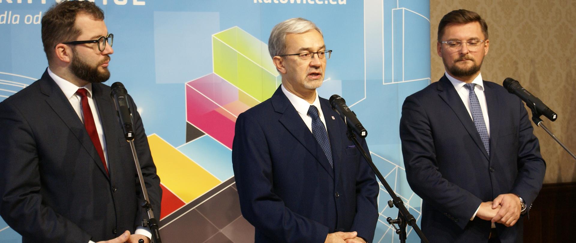 Na tle ścianki miasta Katowic przed mikrofonami od lewej stoją: wiceminister Grzegorz Puda, minister Jerzy Kwieciński oraz prezydent miasta Katowice Marcin Krupa