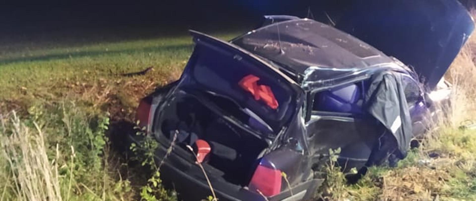 kadr przedstawia uszkodzony pojazd znajdujący się poza drogą. pora nocna.