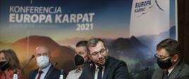 Grupa osób siedzi przy stole wśród nich minister Puda w tle widać napis Konferencja Europa Karpat 2021