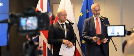 Marek Zagórski, minister cyfryzacji i Jonathan Knott - brytyjski ambasador w Polsce przemawiają do mikrofonów. W tle flagi Wielkiej Brytanii, Polski i UE.