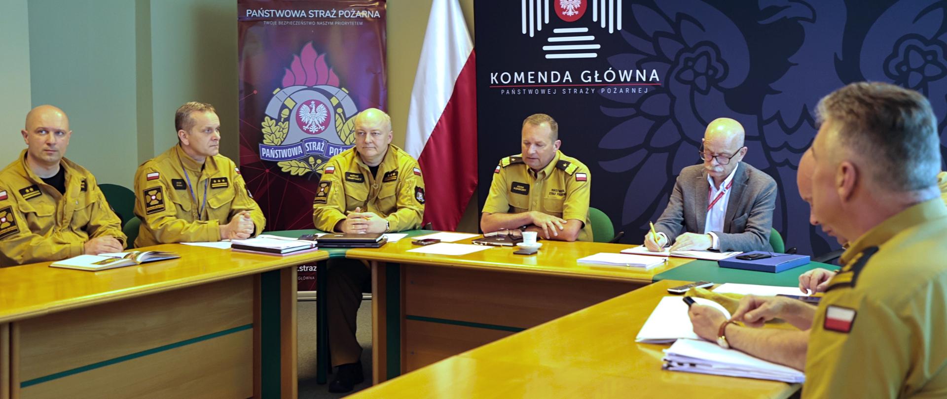Zastępca komendanta głównego i sześciu oficerów z KG PSP oraz mężczyzna w ubraniu cywilnym siedzący przy stole. 
