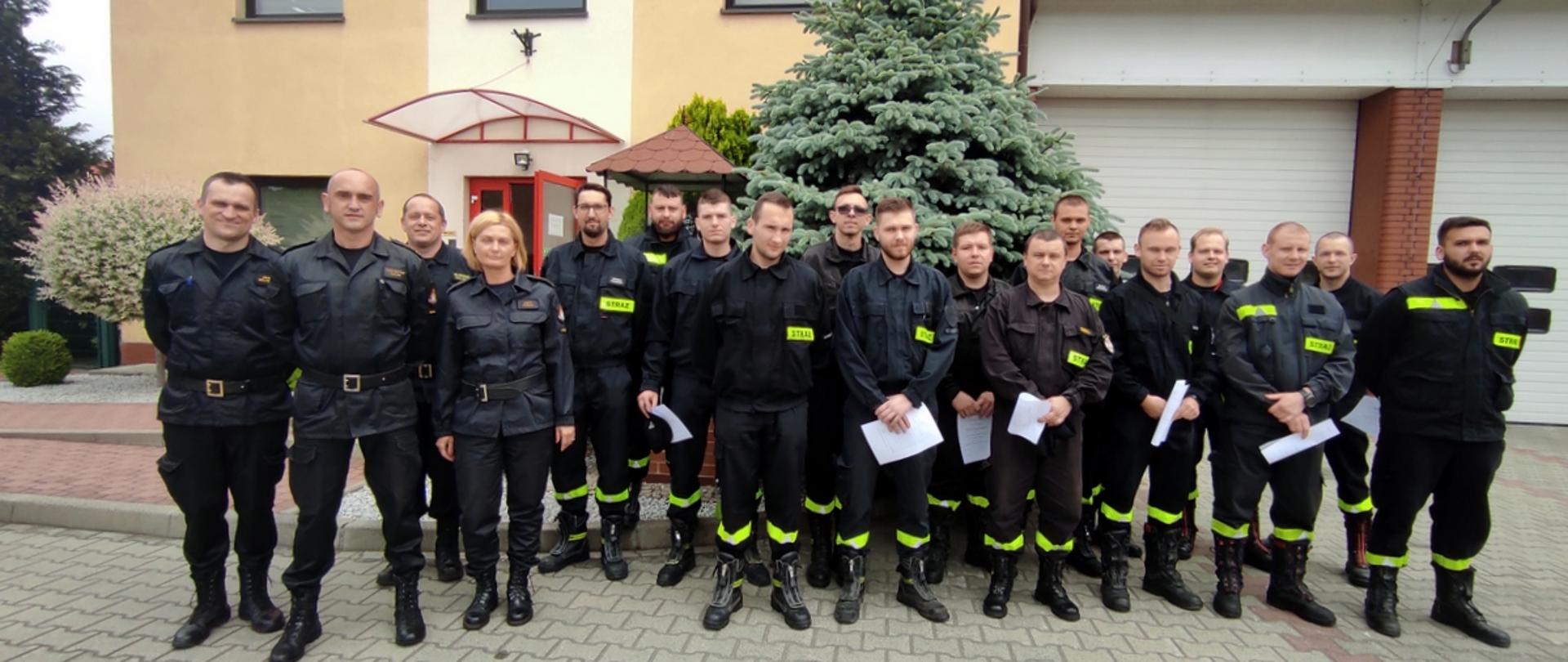 na zdjęciu widać strażaków OSP oraz strażaków PSP z komisji egzaminacyjnej przed budynkiem oławskiej komendy PSP. Strażacy są w umundurowaniu koszarowym, trzymają zaświadczenia o ukończonym szkoleniu dla dowódców OSP