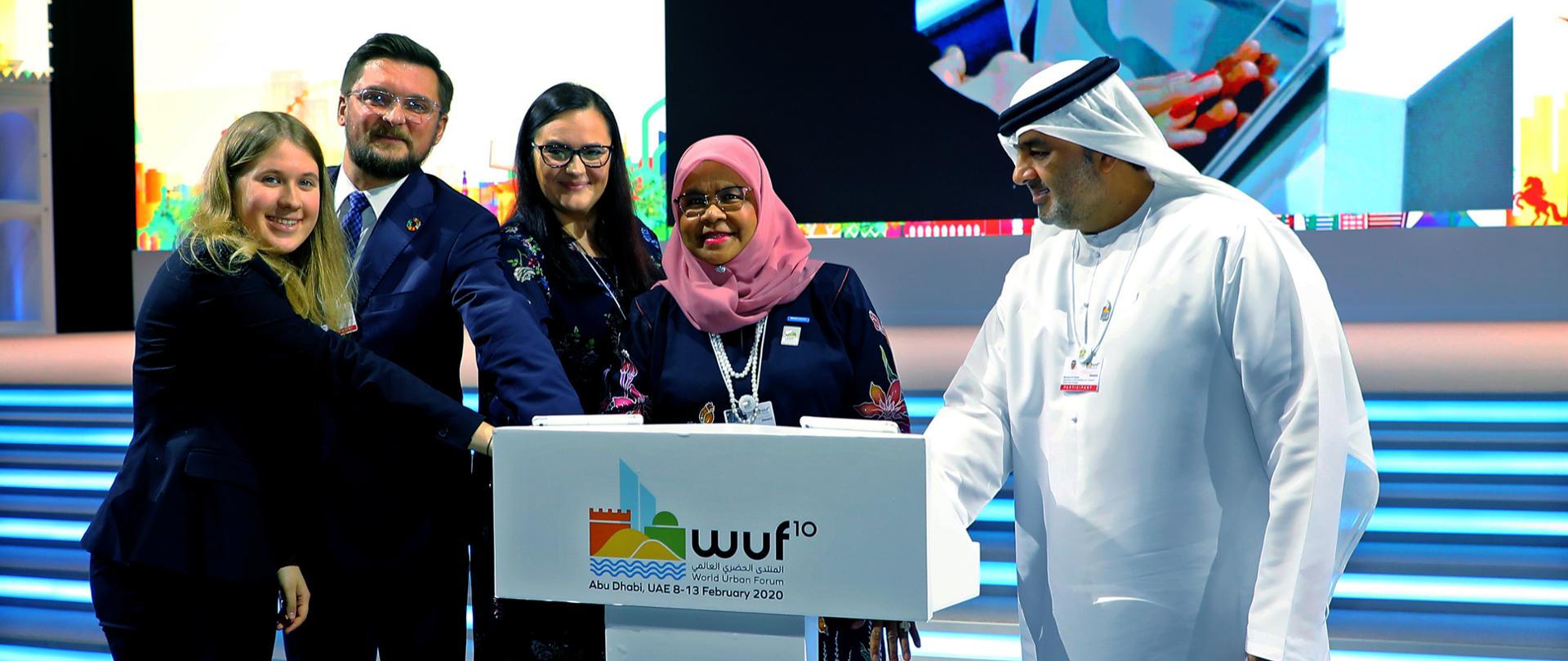 w symbolicznym geście współorganizacji wydarzenia na pulpicie trzymają złożone ręce kilka osób w tym dyrektor UN-Habitat M.M. Sharif, wiceminister Małgorzata Jarosińska-Jedynak i prezydent Katowic Marcin Krupa