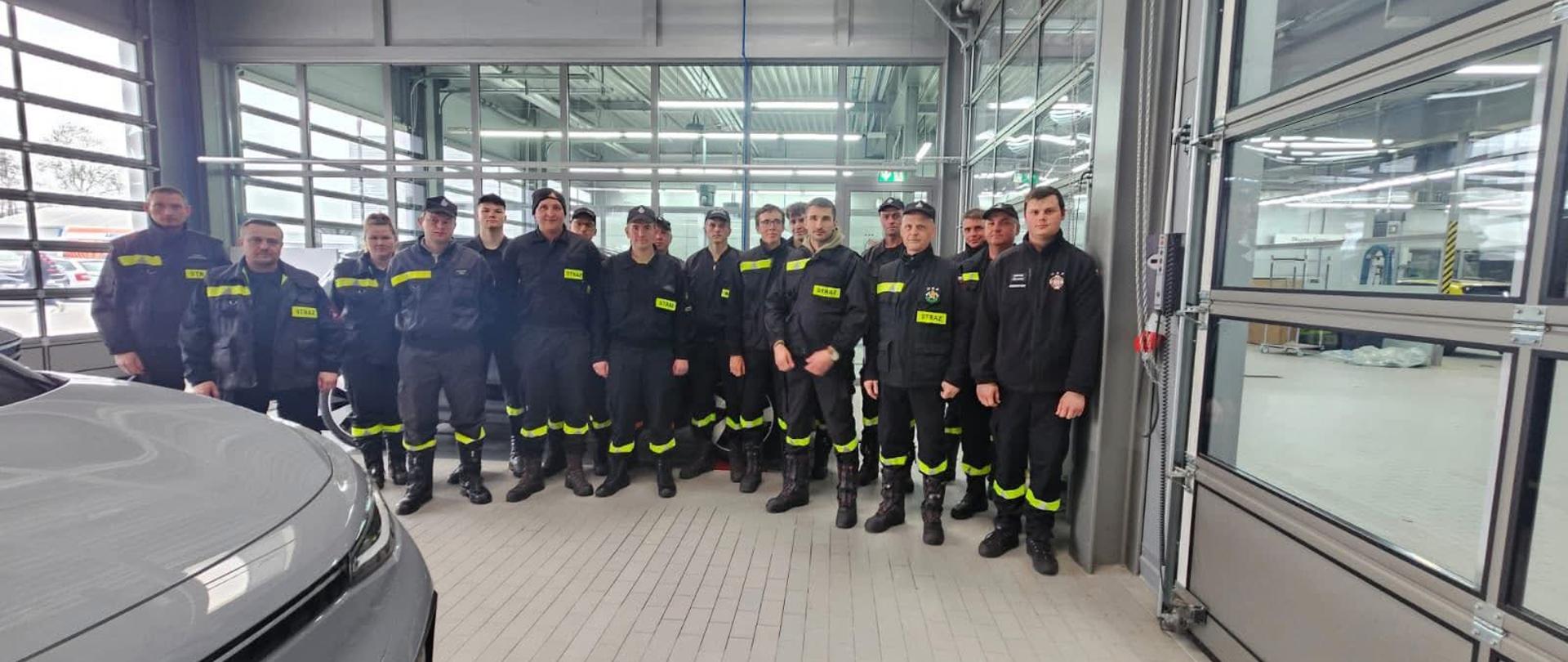 Na zdjęciu ustawieni są strażacy w ubraniach koszarowych na hali 