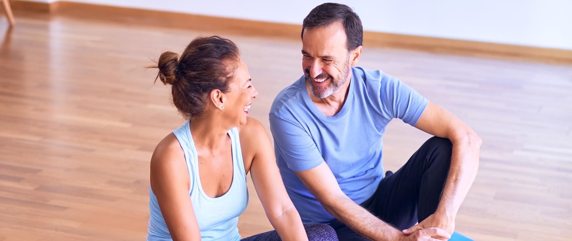 Uśmiechnięci kobieta i mężczyzna siedzący na macie do ćwiczeń.