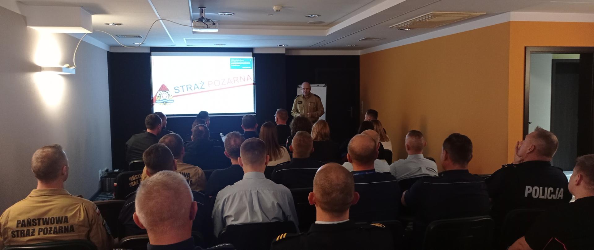 Spotkania dla dyżurnych organizowane przez OUW - zdjęcie przedstawia prezentację przygotowaną mł.kpt. Jarosława Buhla. Na zdjęciu widać również uczestników szkolenia siedzących na wprost prowadzącego.