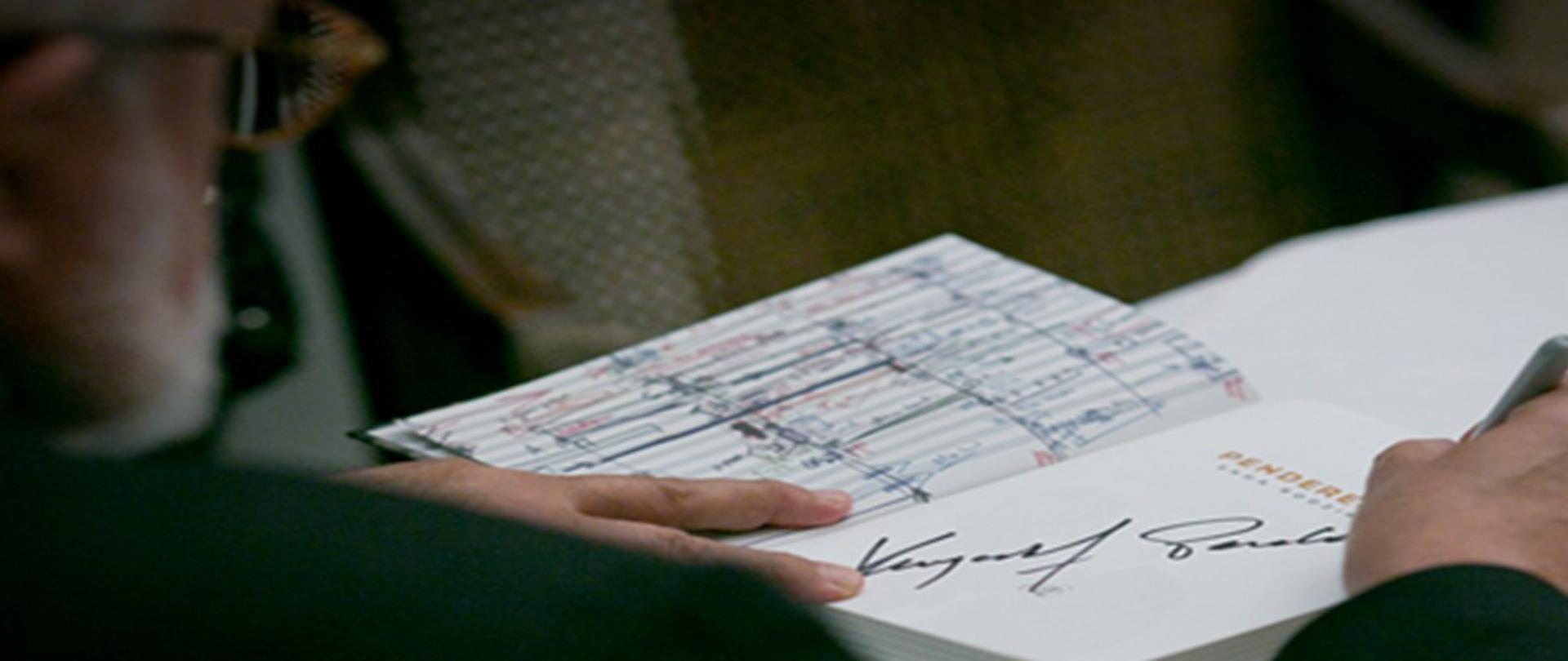 Plakat z wydarzeniem - Informacją dotyczącą 5 rocznicy śmierci prof. Krzysztofa Pendereckiego, tłem plakatu jest postać kompozytora, który dokonuje wpisu do książki