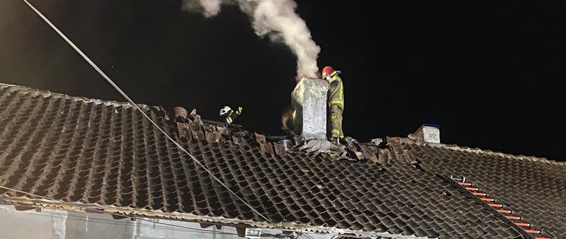Na zdjęciu widać budynek, w którym doszło do zdarzenia, strażaków podczas akcji gaśniczej oraz strażaka badającego temperaturę przewodu kominowego.