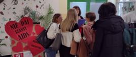 Grupa uczniów uczestniczy w quizie wiedzy. Przy stoisku wyeksponowana wystawa z czerwonych serc z napisem „Nie daj szansy AIDS”.