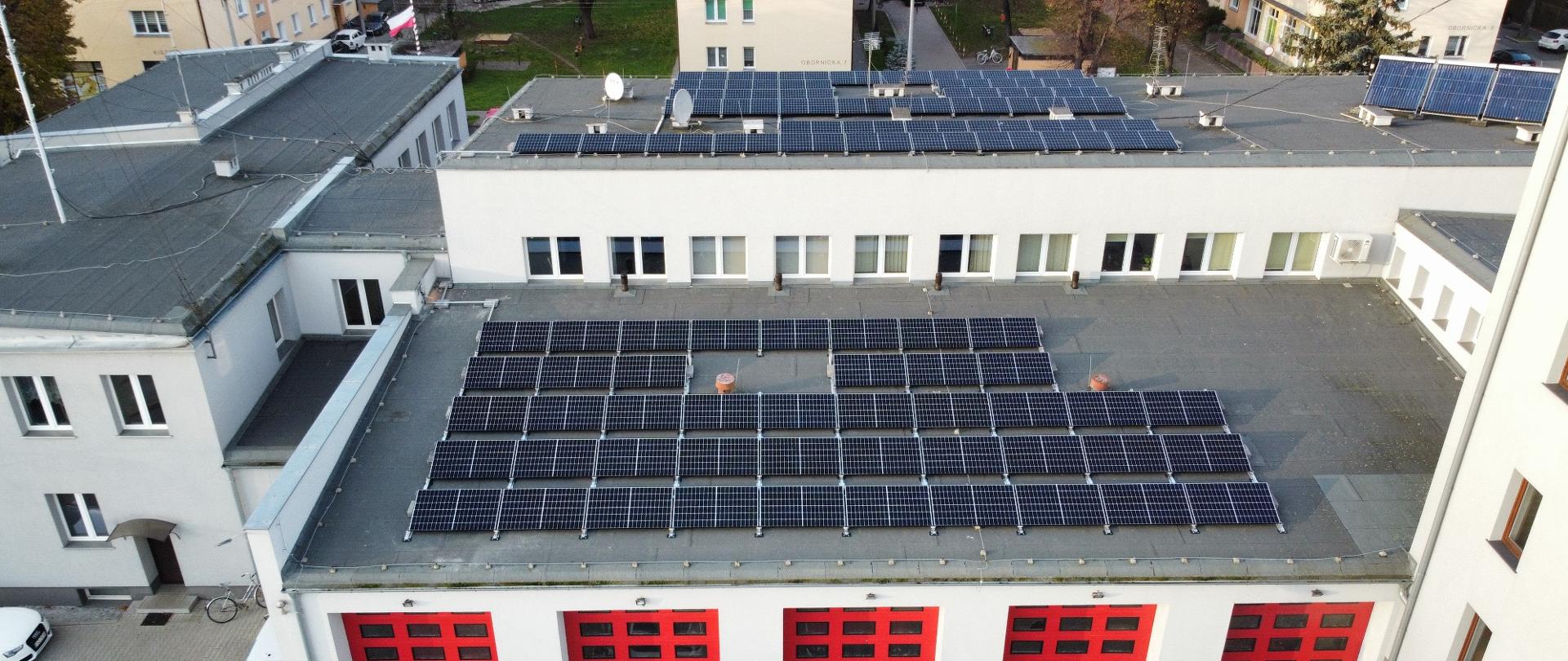 Widać zamontowane panele fotowoltaiczne na dachu budynku komendy straży pożarnej, widok z lotu ptaka 