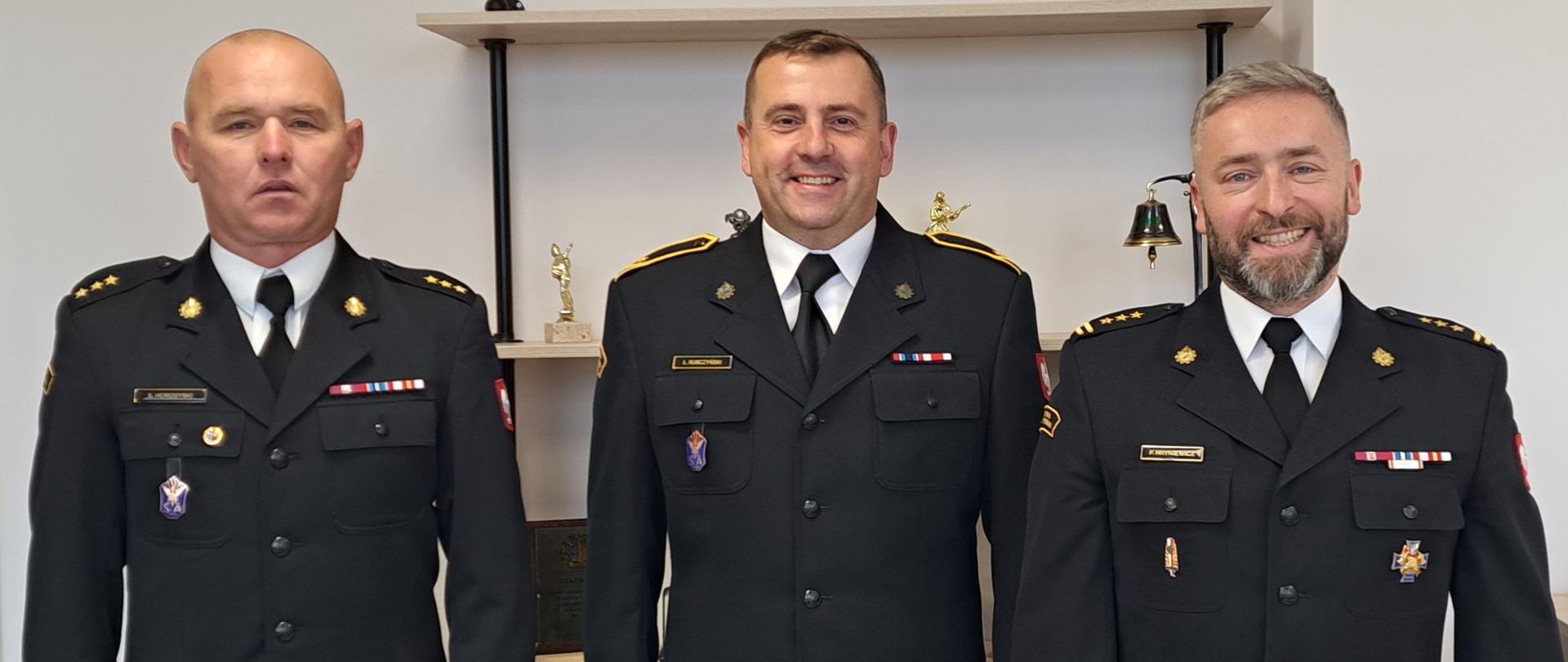 strażak otrzymujący nagrodę z Komendantem Powiatowym i Dowódcą Jednostki Ratowniczo Gaśniczej