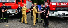 Na zdjęciu widoczni strażacy z którymi wita się Z-ca MKW. Strażacy stoją na tle wozów ratowniczo gaśniczych.
