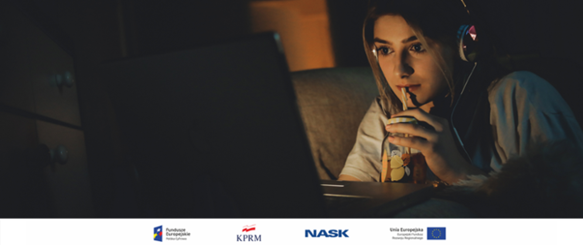 Młoda dziewczyna - nastolatka leży na łóżku w ciemnym pokoju i ogląda coś na laptopie.